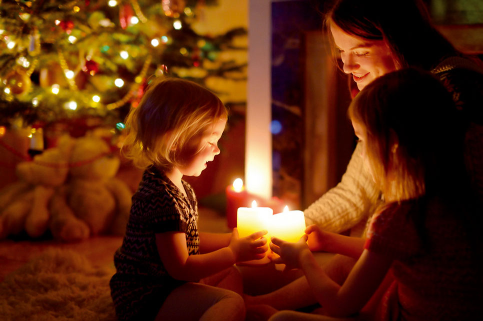 Mutter mit zwei Kindern und Kerzen vor dem Weihnachtsbaum