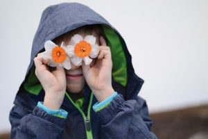 Junge hält sich zwei Narzissen-Blüten vor die Augen