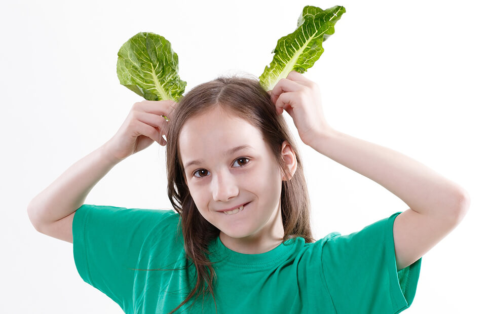 Mädchen hält sich Salatblätter als Hasenohren an den Kopf