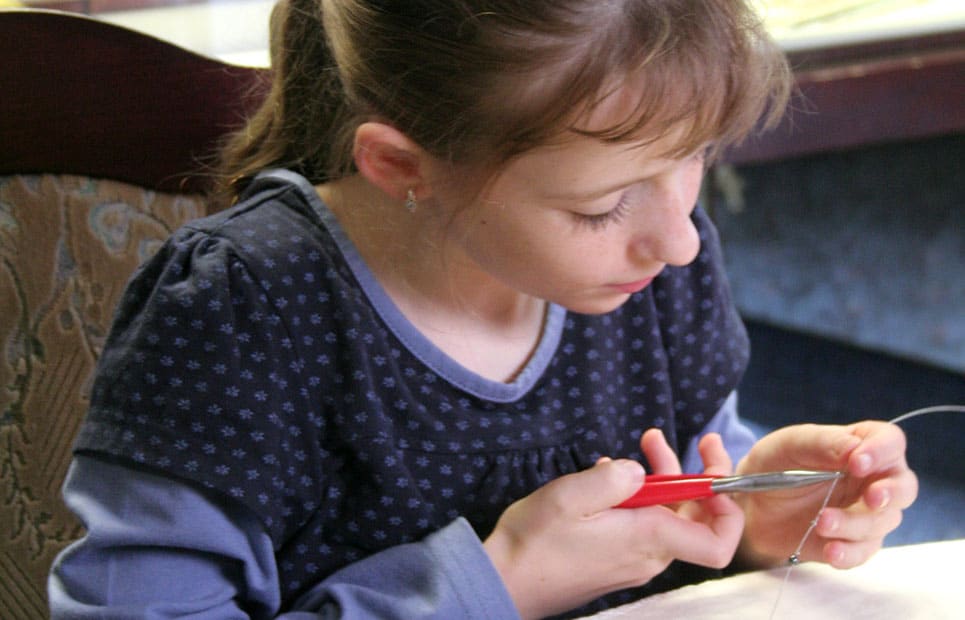 Ein Mädchen fertigt mit Hilfe einer Zange und Draht ein Schmuckstück an