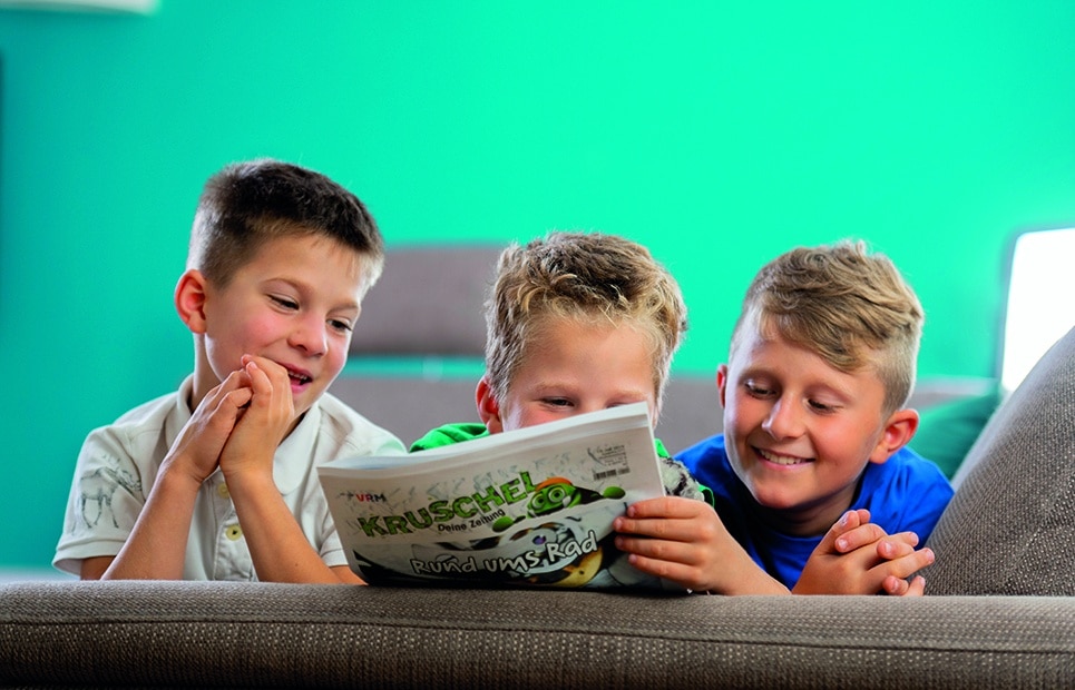 Man sieht drei Jungen mit der Kruschel Zeitschrift auf dem Sofa liegen