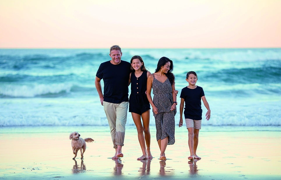 Man sieht eine Familie mit zwei Kindern und Hund am Strand spazieren